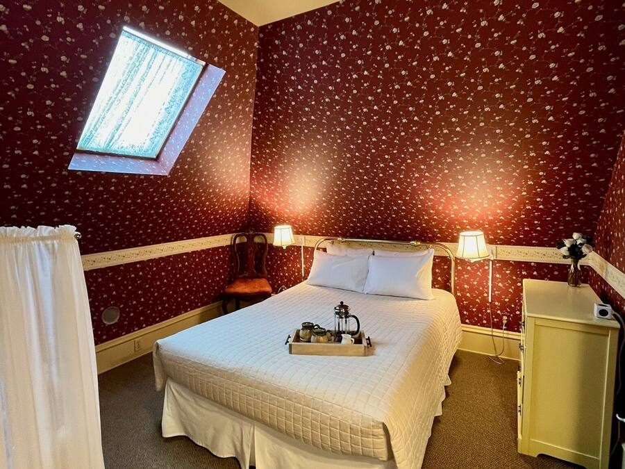 A hotel room with a bed, bedside lamps, a small table with a tray, a window, and a wardrobe.