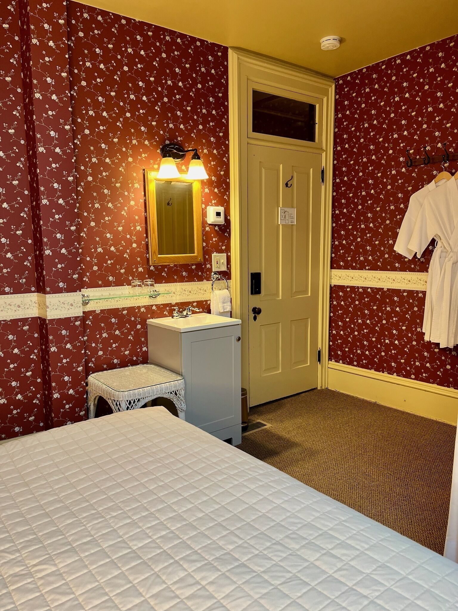 Una habitación de hotel con una cama, una mesita de noche, un lavamanos y un espejo.
