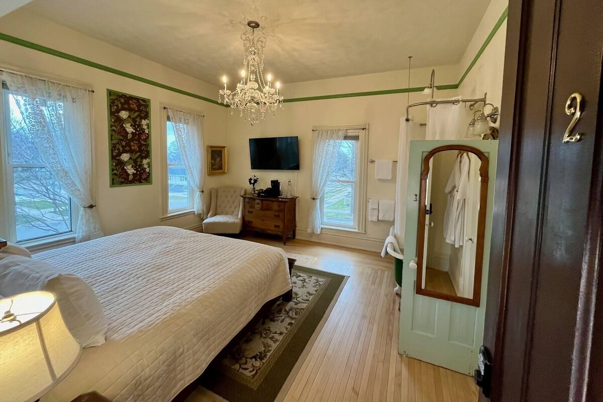 A bedroom with a large bed, a chandelier, a dresser, a television, and a mirror.