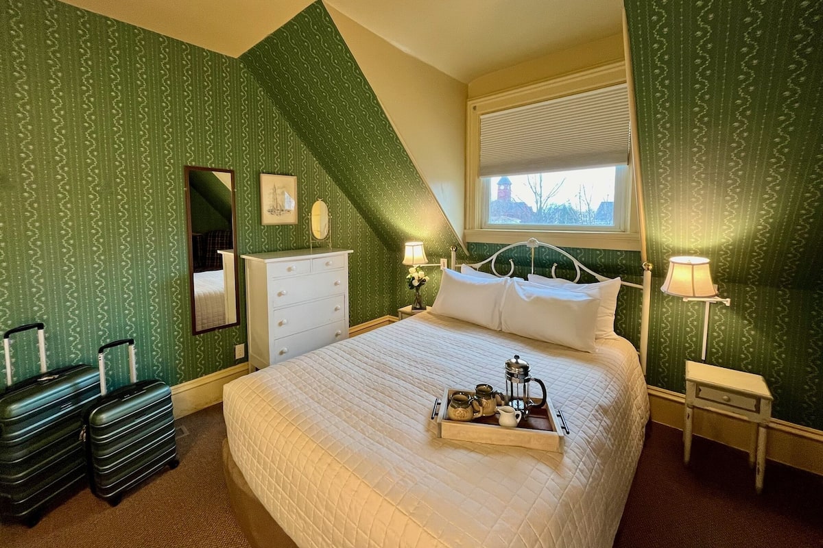 A bedroom with a bed, a dresser, a mirror, a window, and two suitcases.