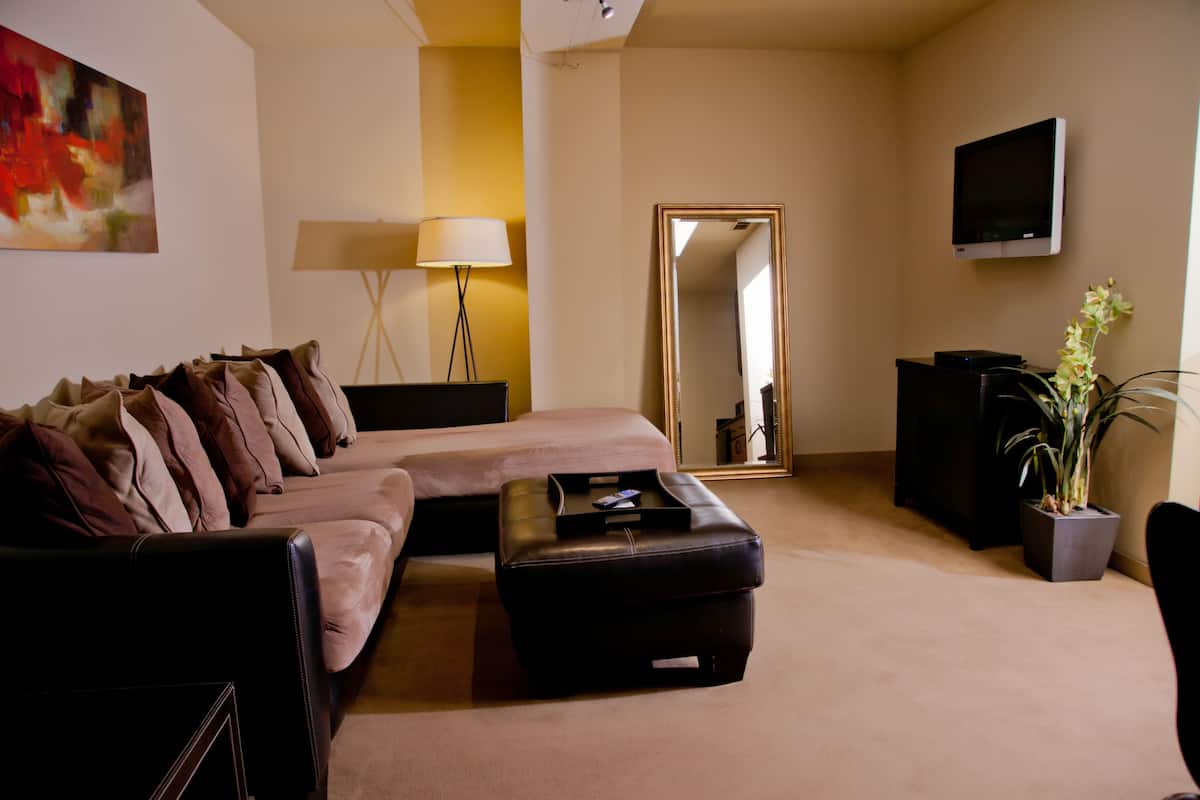 A modern hotel room with a large bed, a sofa, a small table, a lamp, a TV, and a potted plant.