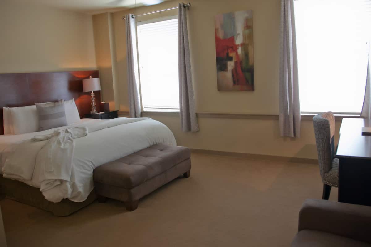A hotel room with a large bed, a bedside table with a lamp, a chair, and a painting on the wall.