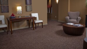 Habitación de hotel con una mesa de madera, dos sillas, una mesita redonda y piso alfombrado.