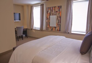 A hotel room with a large bed, a desk with a chair, a television mounted on the wall, and a window with curtains. - V Boutique Hotel (Corpus Christi)