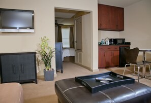 A hotel room with a TV, a bed, a kitchenette, a seating area with a tray, and a potted plant. - V Boutique Hotel (Corpus Christi)