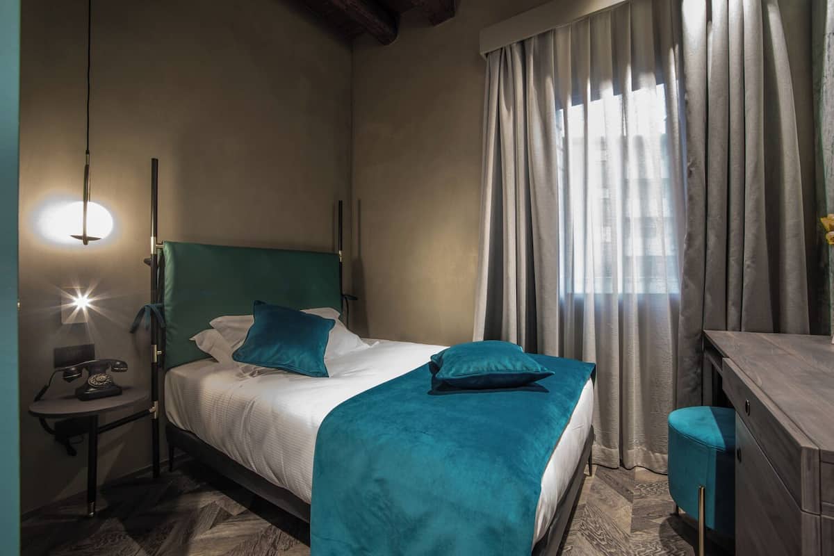 Una cama bien hecha con ropa de cama color turquesa, una lámpara de noche y un teléfono antiguo sobre la mesita.
