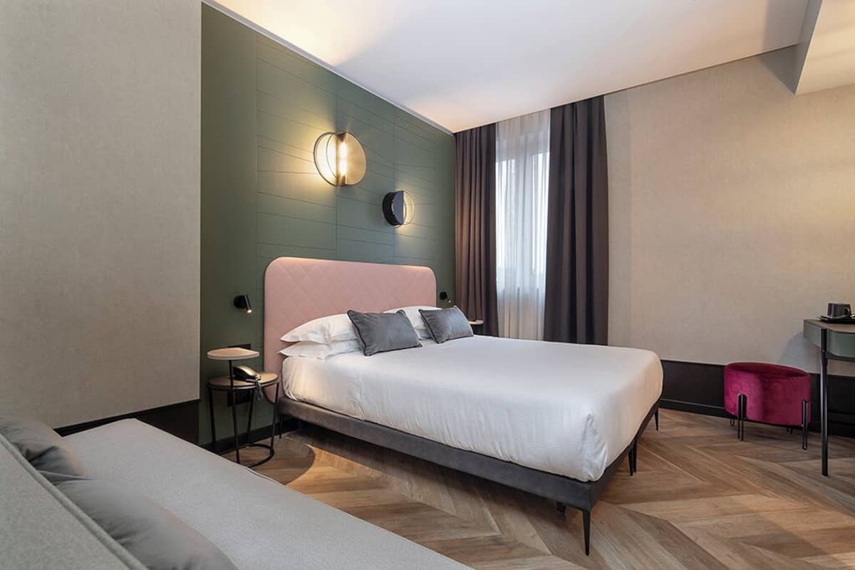 Una habitación de hotel moderna con una cama grande, una mesita pequeña, una silla y un reposapiés rojo.