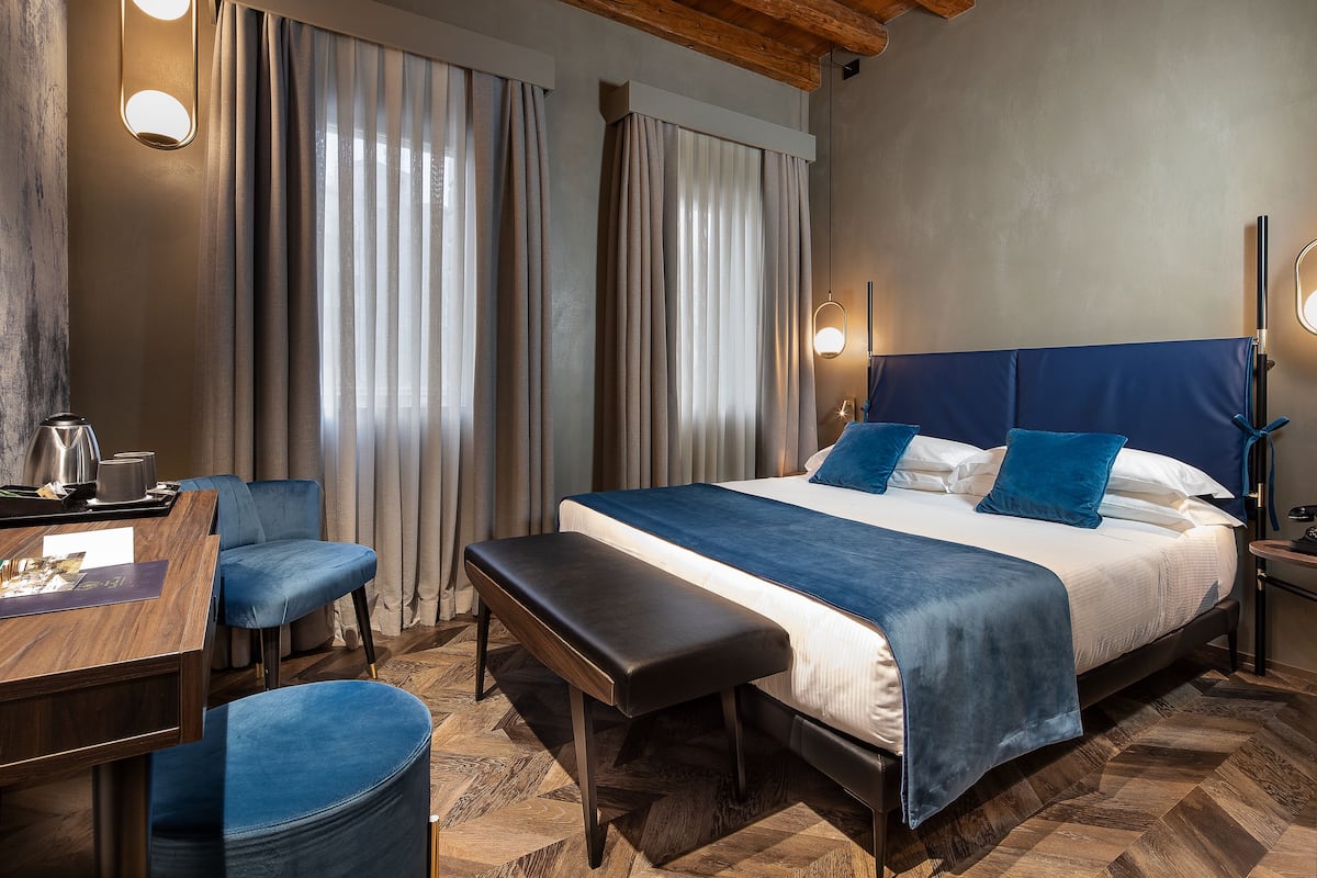 Una habitación de hotel con una cama grande, un escritorio con silla, un banco y una mesita de noche.