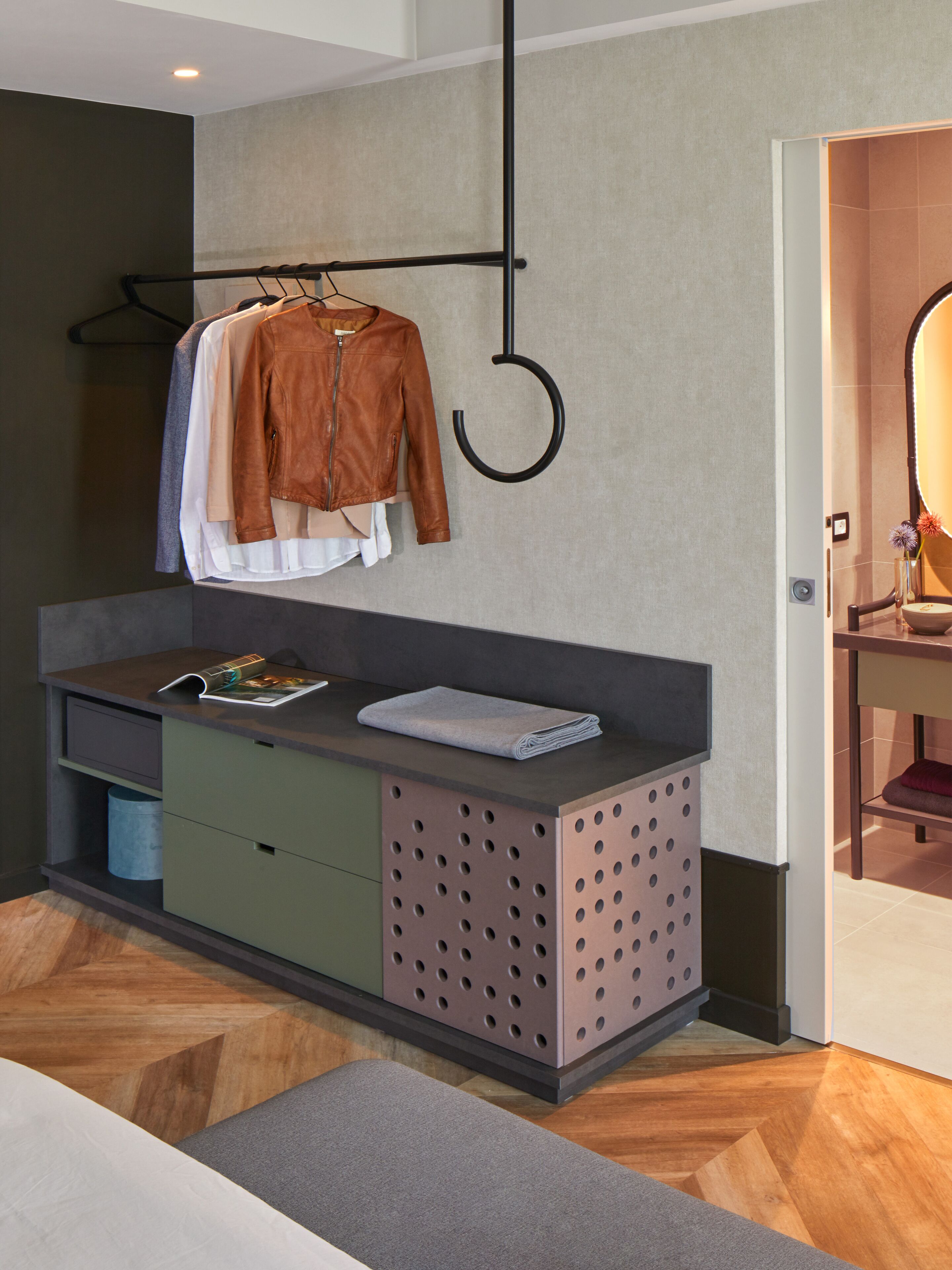 A modern bathroom with a wooden floor, a vanity with a mirror, and a towel rack with clothes.