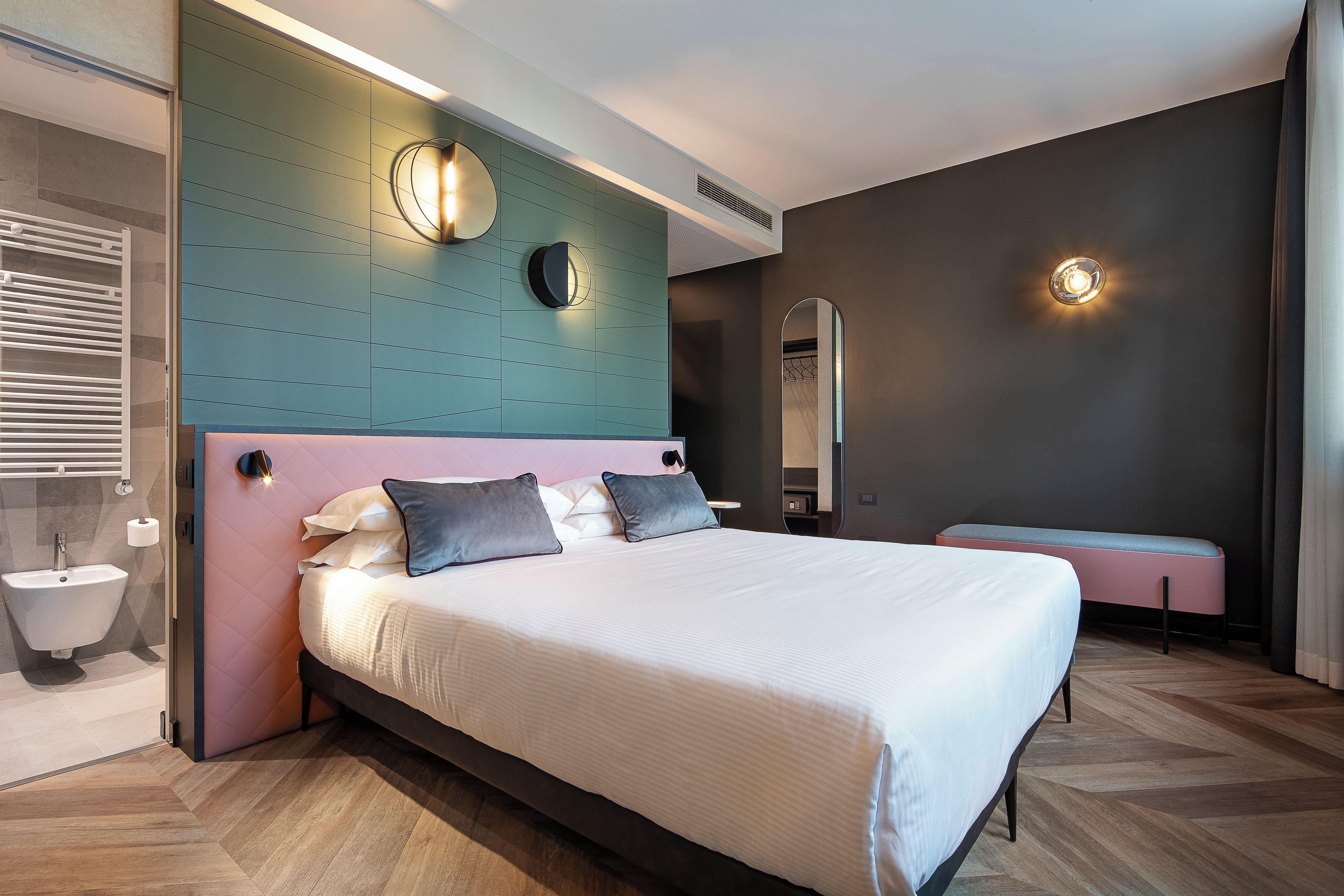 A modern bedroom with a large bed, a bedside table, a wall-mounted mirror, and a built-in heater.