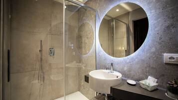 Un baño moderno con ducha envuelta en cristal, un espejo redondo y un lavamanos blanco.