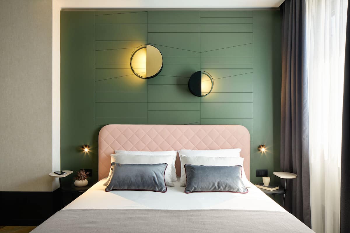 Un dormitorio moderno con una pared de acento verde, un cabecero rosa y dos mesitas de noche con lámparas.