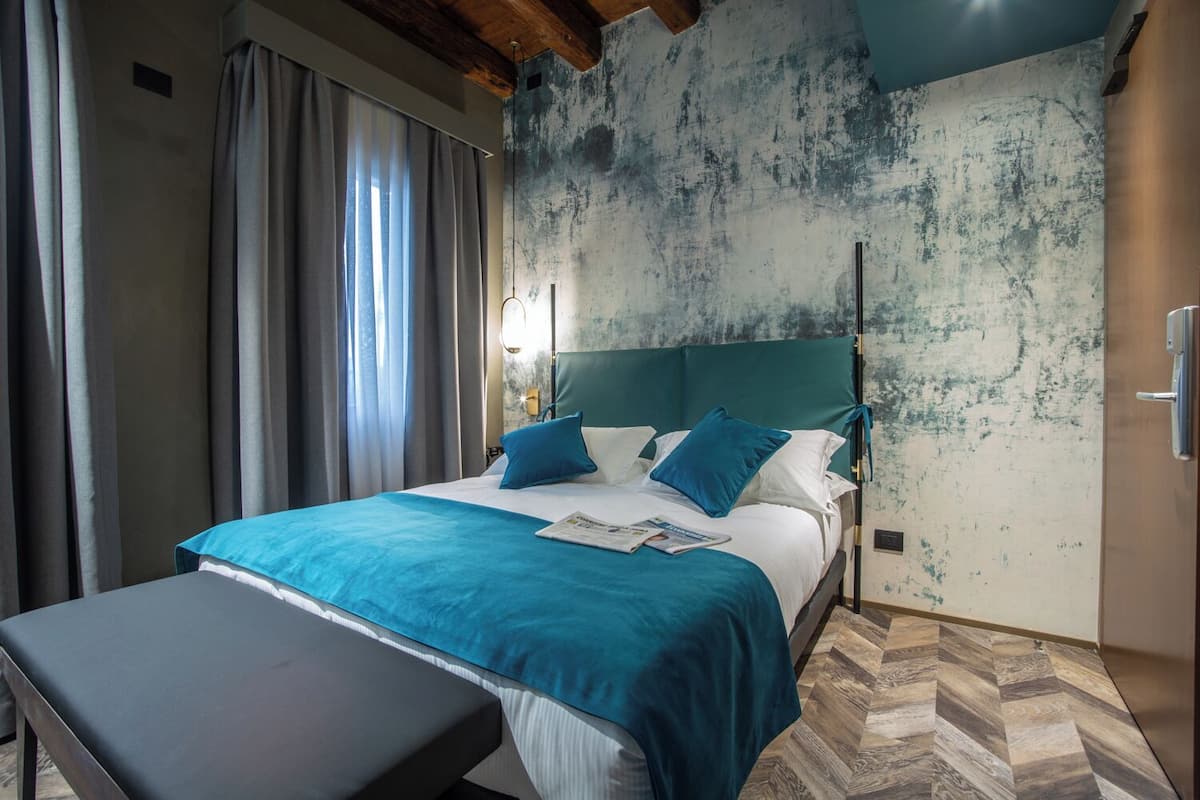 Un dormitorio con cama, una banca, una ventana con cortinas y una pared con textura.