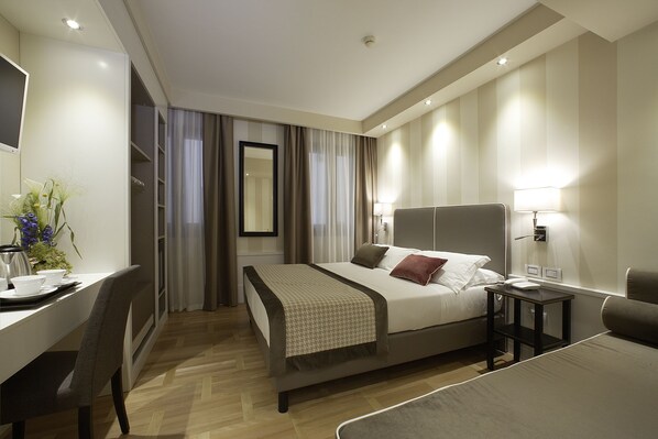 Una habitación de hotel moderna con cama, mesita de noche, lámpara y un escritorio con silla.