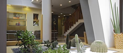 A modern lobby with a cactus garden, a staircase, and a reception area with shelves.