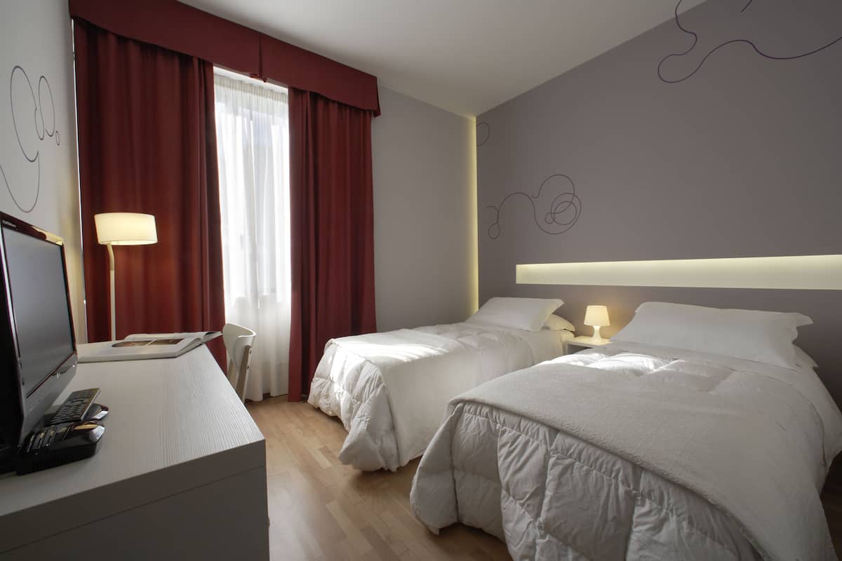 Habitación de hotel con dos camas, un escritorio con computadora y una ventana con cortinas.