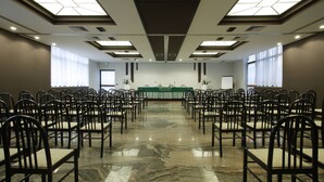 Konferenssisali, jossa on riveittäin tuoleja ja edessä lava, jonka taustalla on vihreä seinä.
