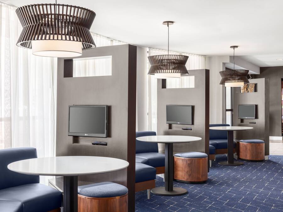 A modern hotel lobby with round tables, blue cushioned seating, and large pendant lights.