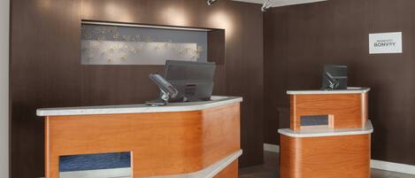 A reception desk with a laptop, a sign reading "Marriott Bonvoy," and a wall-mounted artwork.