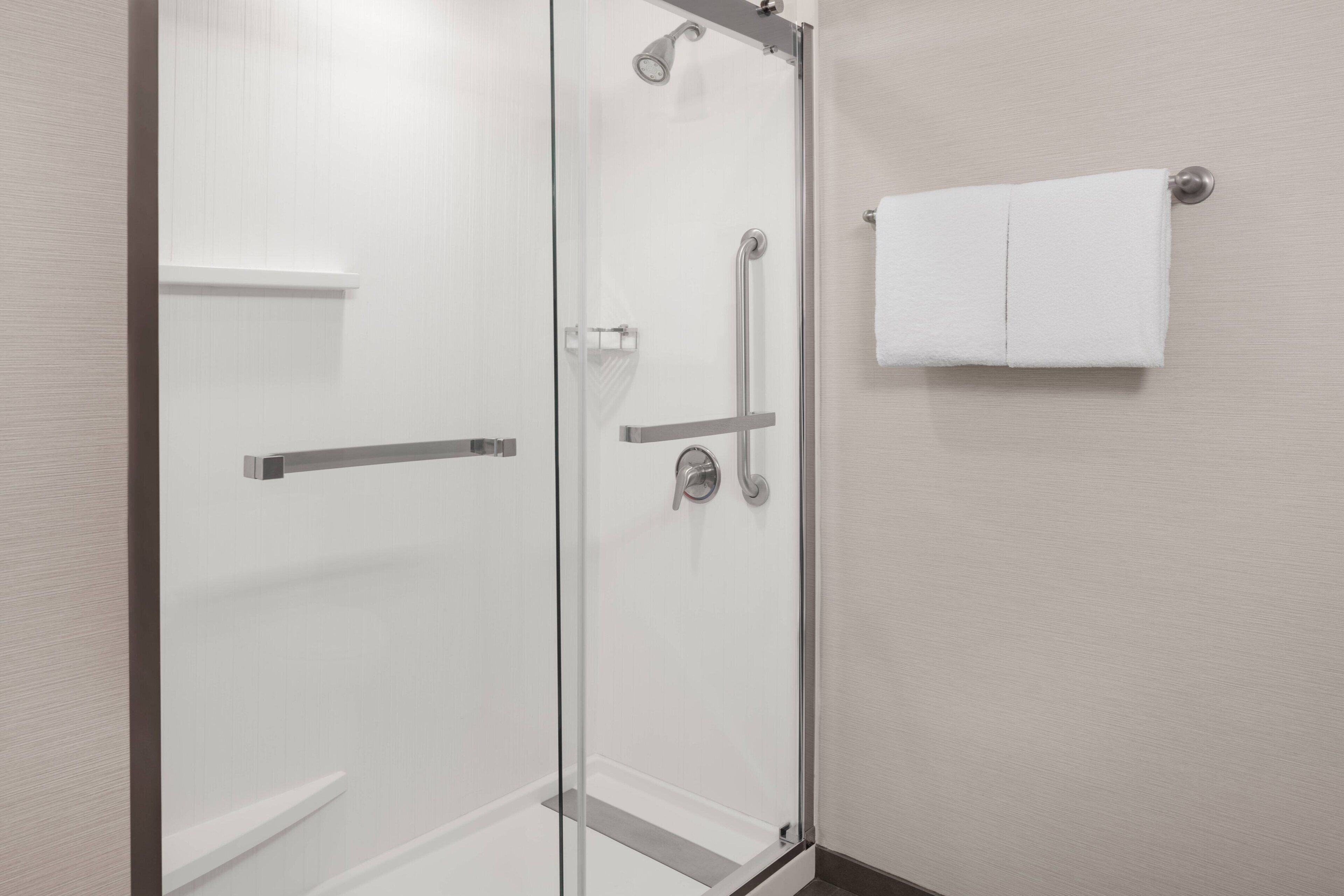 Un baño moderno con cabina de ducha de vidrio, una toalla blanca colgada en un toallero de pared y un inodoro a la vista.