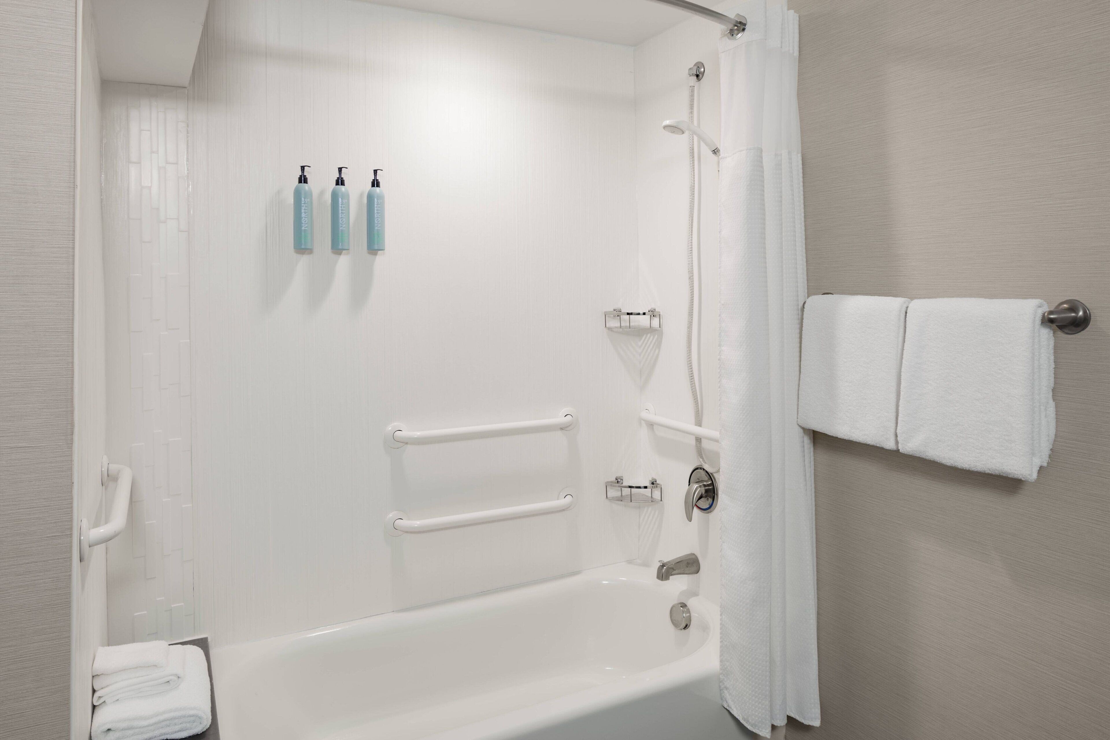 A modern bathroom with a bathtub, grab bars, a towel rack, and a shower curtain.