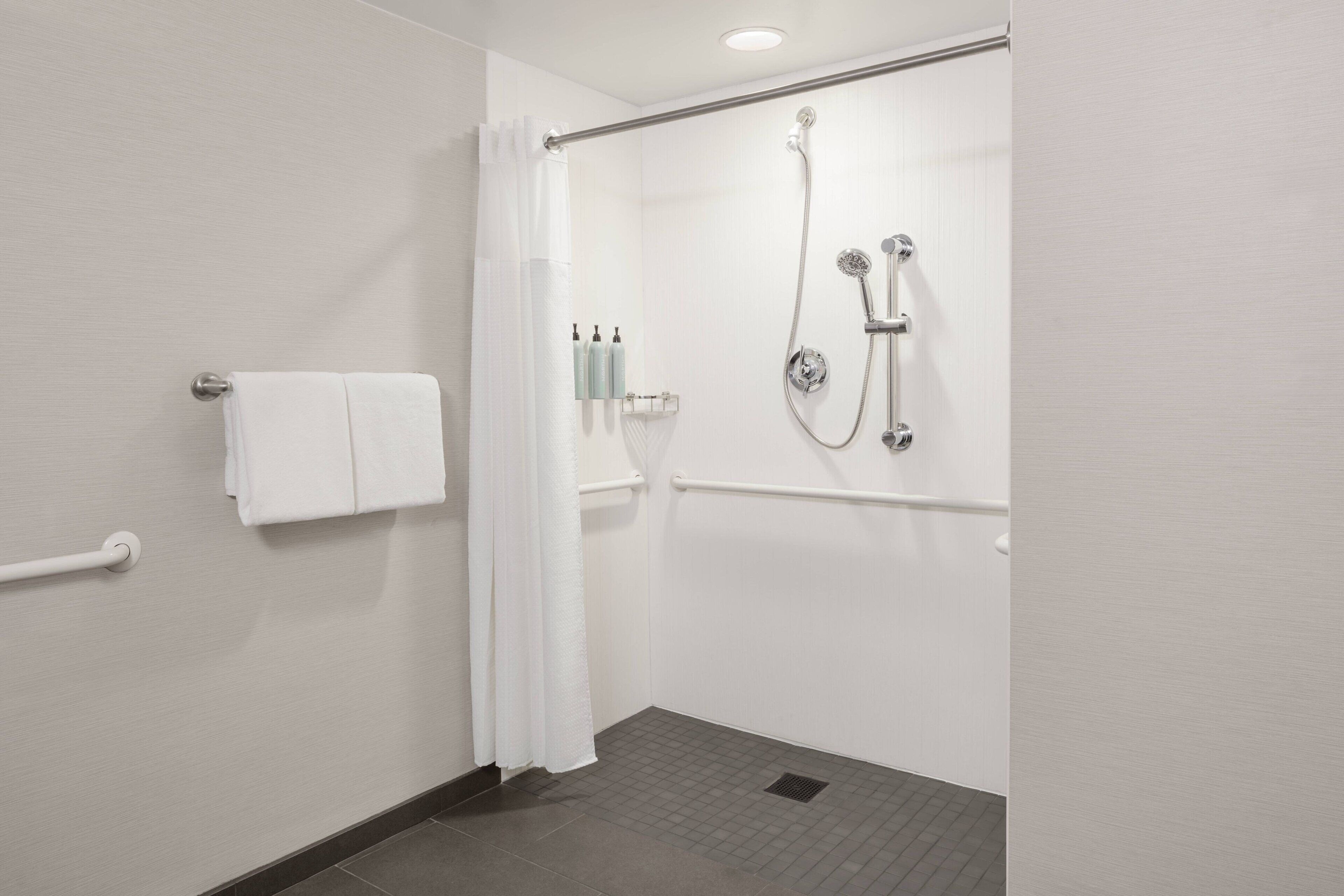A modern bathroom with a shower, grab bar, and towel rack.