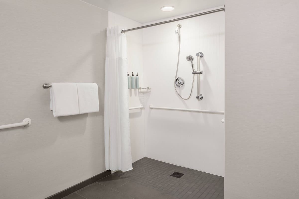 Un baño moderno con ducha, barra de apoyo y toallero.