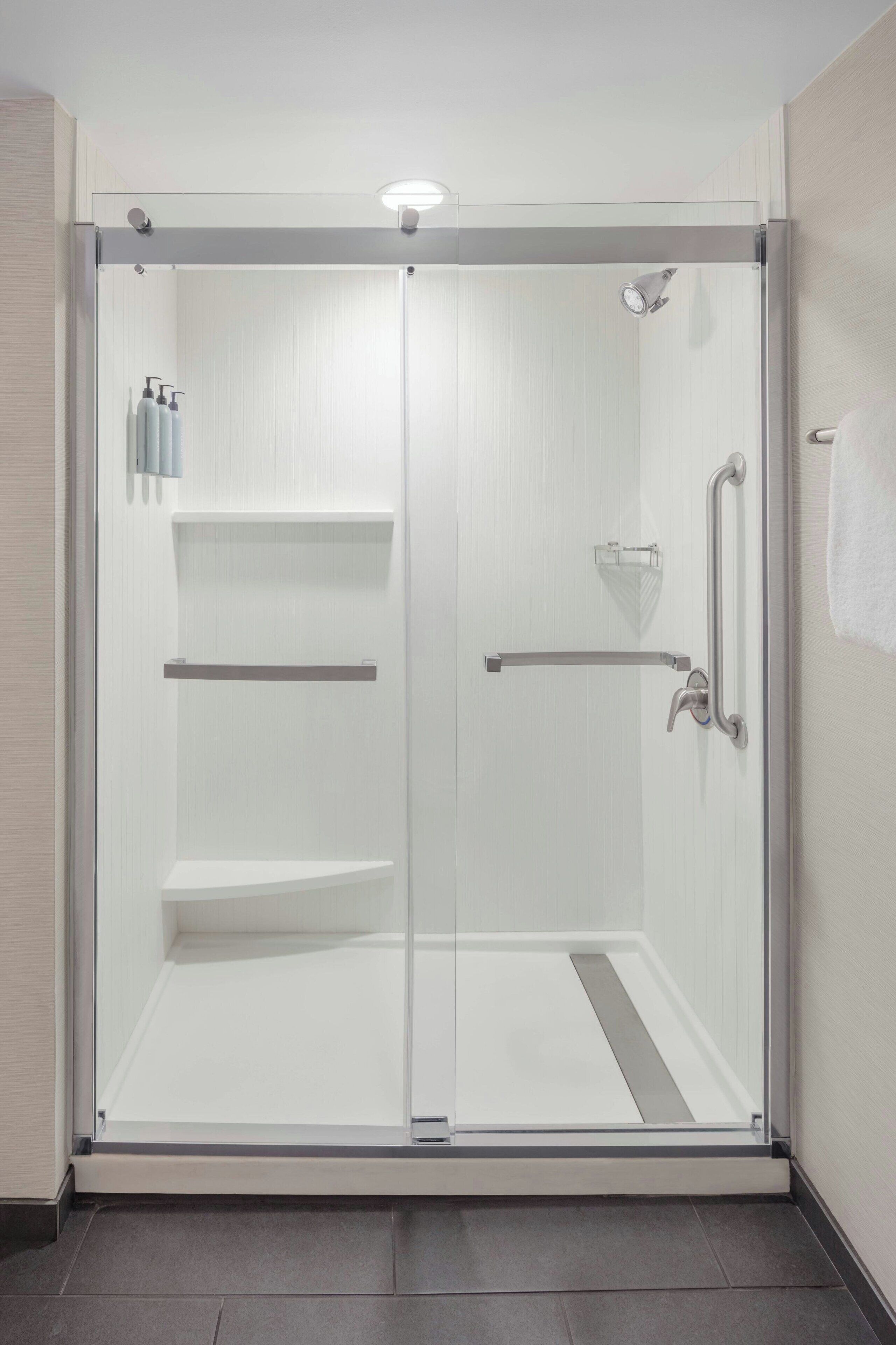 A modern shower enclosure with a glass door, a handrail, and a towel rack.