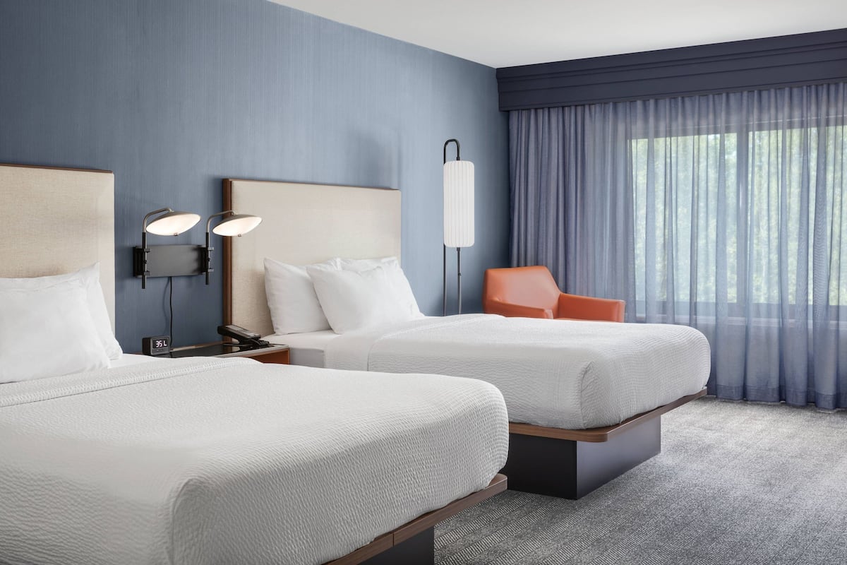 Habitación de hotel con dos camas, una mesita de noche, una lámpara y una silla.