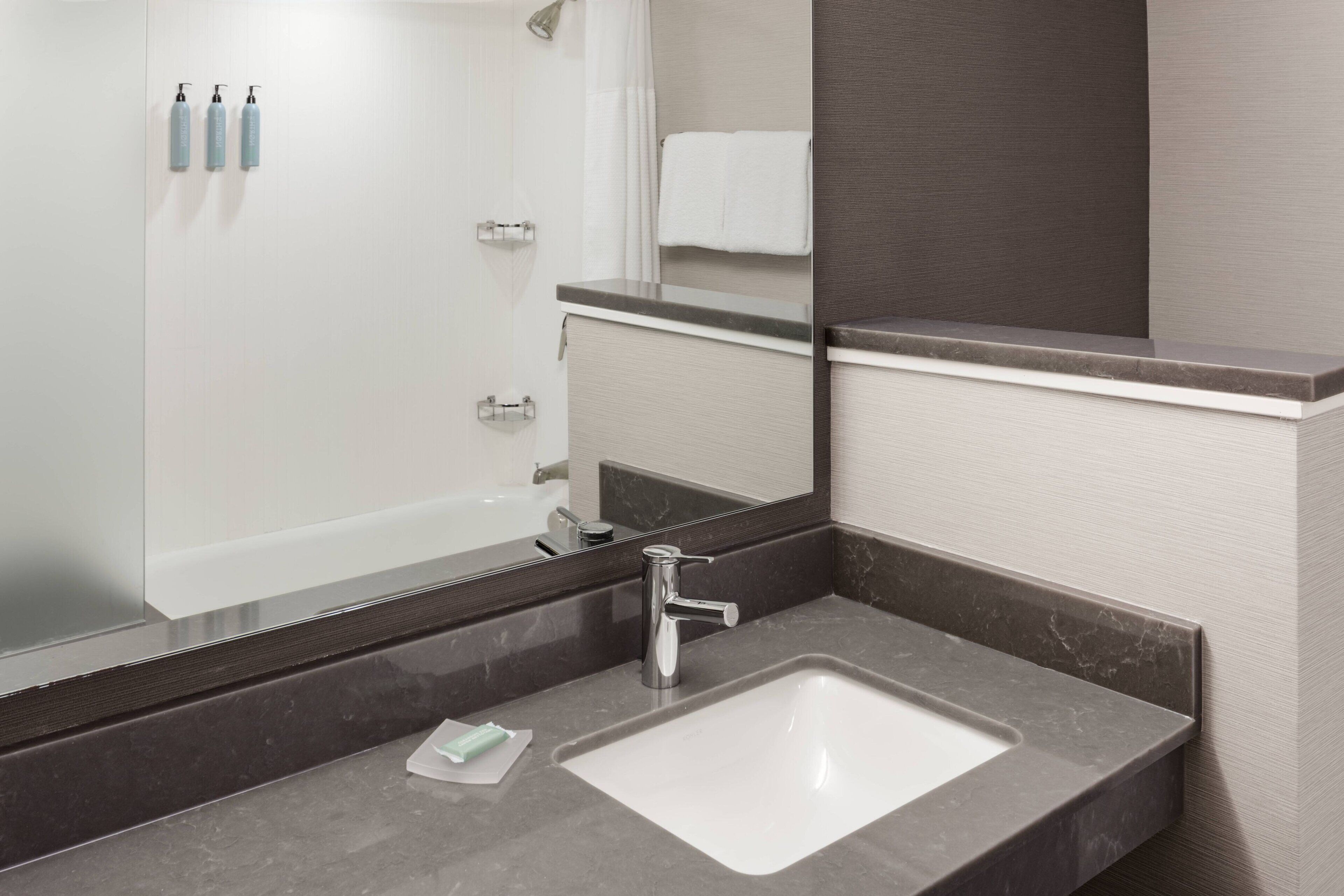 A modern bathroom with a large mirror, a white sink, and a shower area.