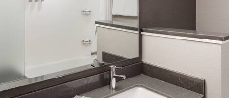 A modern bathroom with a large mirror, a white sink, and a shower area.