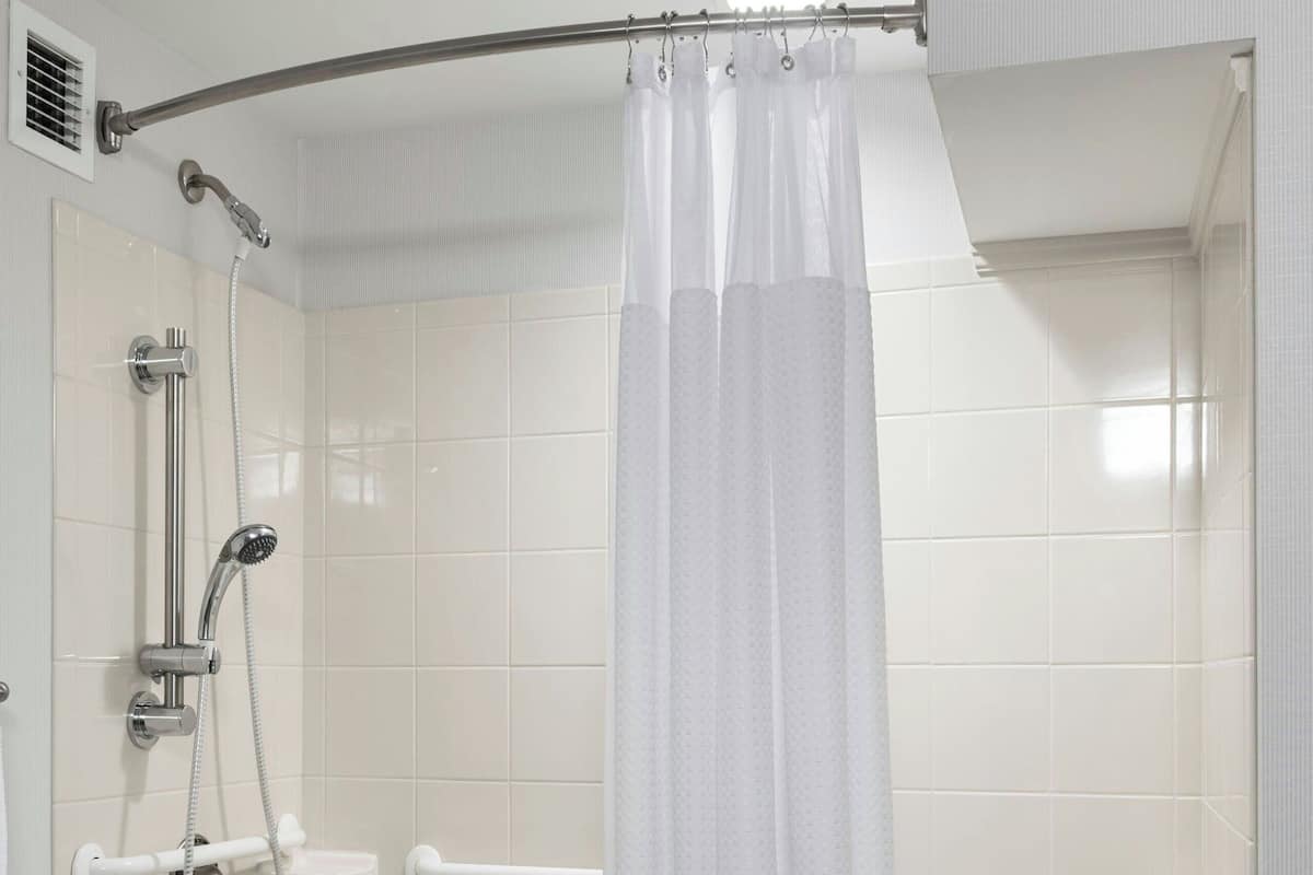 Un baño moderno con ducha a nivel, barras de apoyo, una bañera blanca y un perchero para toallas.