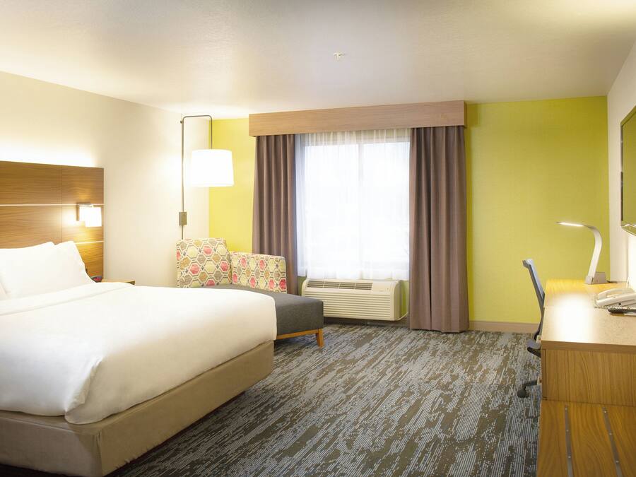 A hotel room with a bed, a desk, a chair, a desk lamp, a TV, and a window with curtains.