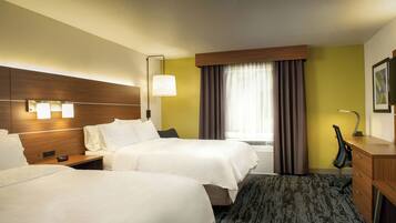 A hotel room with two beds, a desk, a chair, a lamp, and a window with curtains.