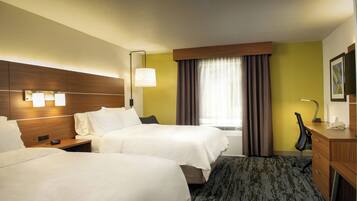 A hotel room with two beds, a desk, a chair, a lamp, and a window with curtains.