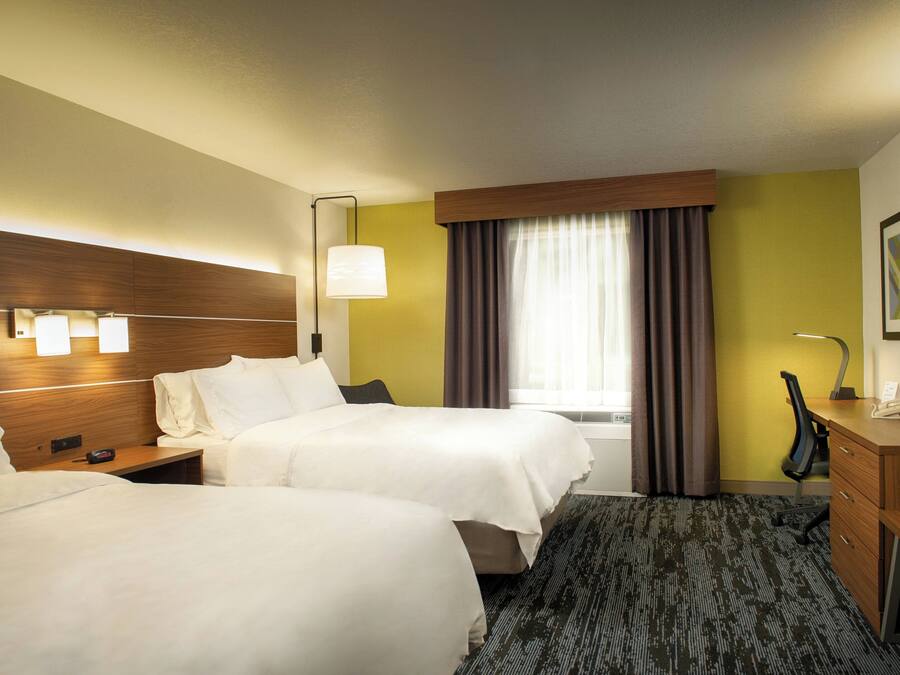 A hotel room with two beds, a desk, a chair, a lamp, and a window with curtains.