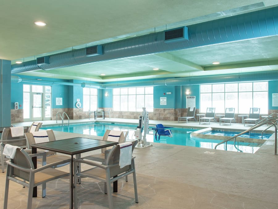A pool area with multiple pools, lounge chairs, and a table with chairs.
