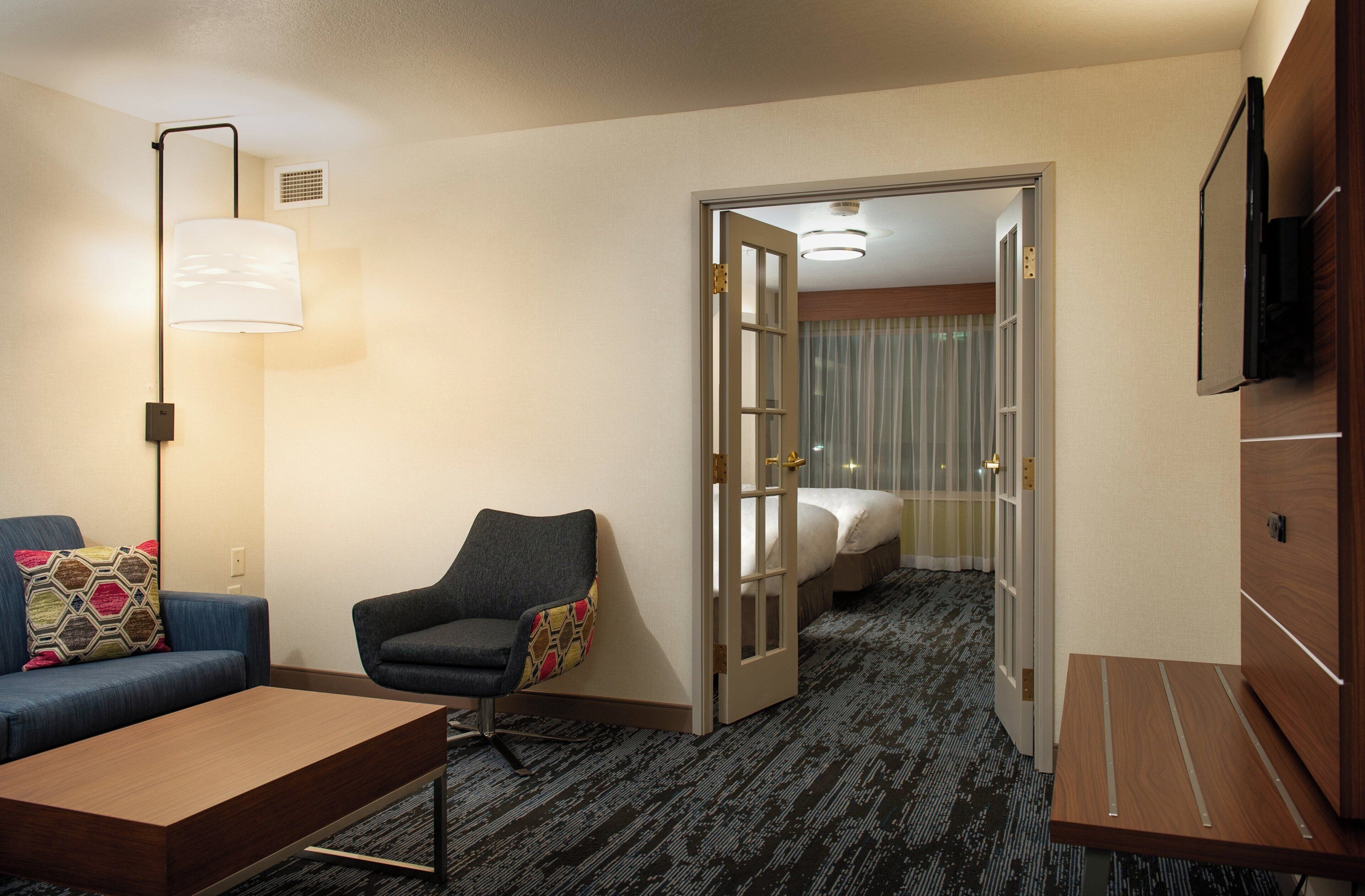 A hotel room with a sofa, armchair, bedside table, and a bed with a curtain.