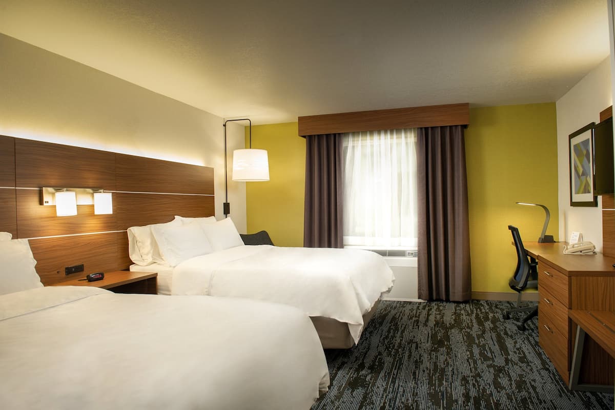 A hotel room with two beds, a desk, a chair, a lamp, and a window with curtains.