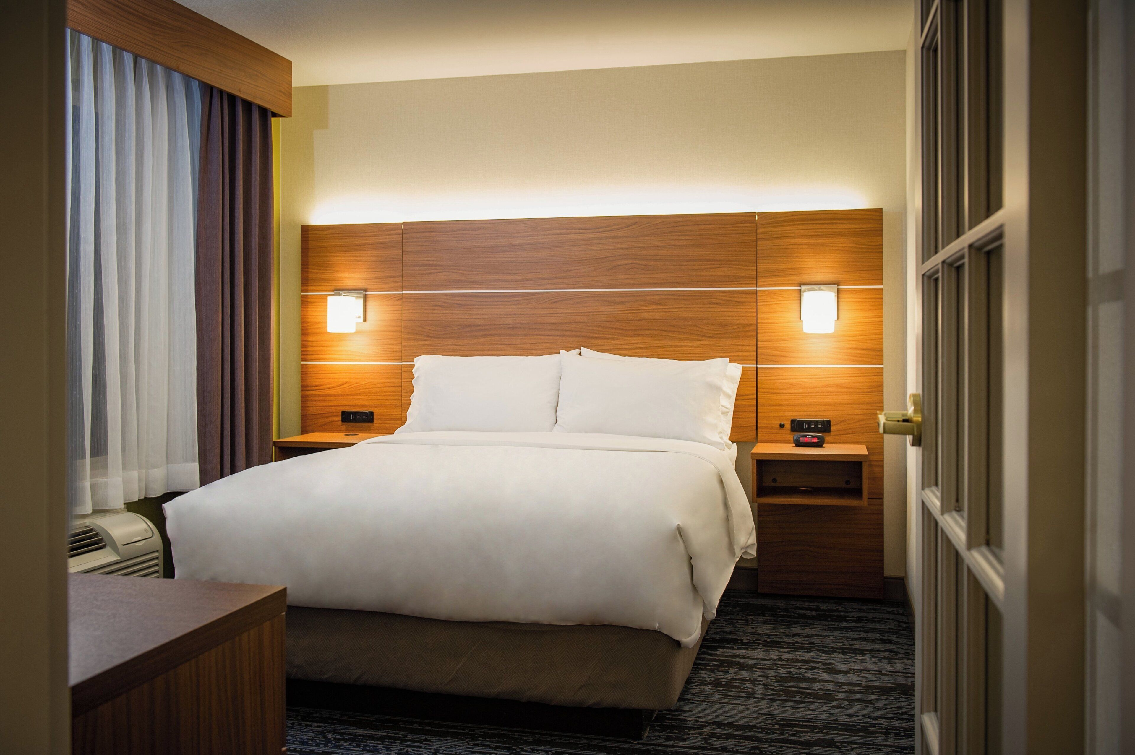 A hotel room with a large bed, two bedside tables, a desk, and a window with curtains.