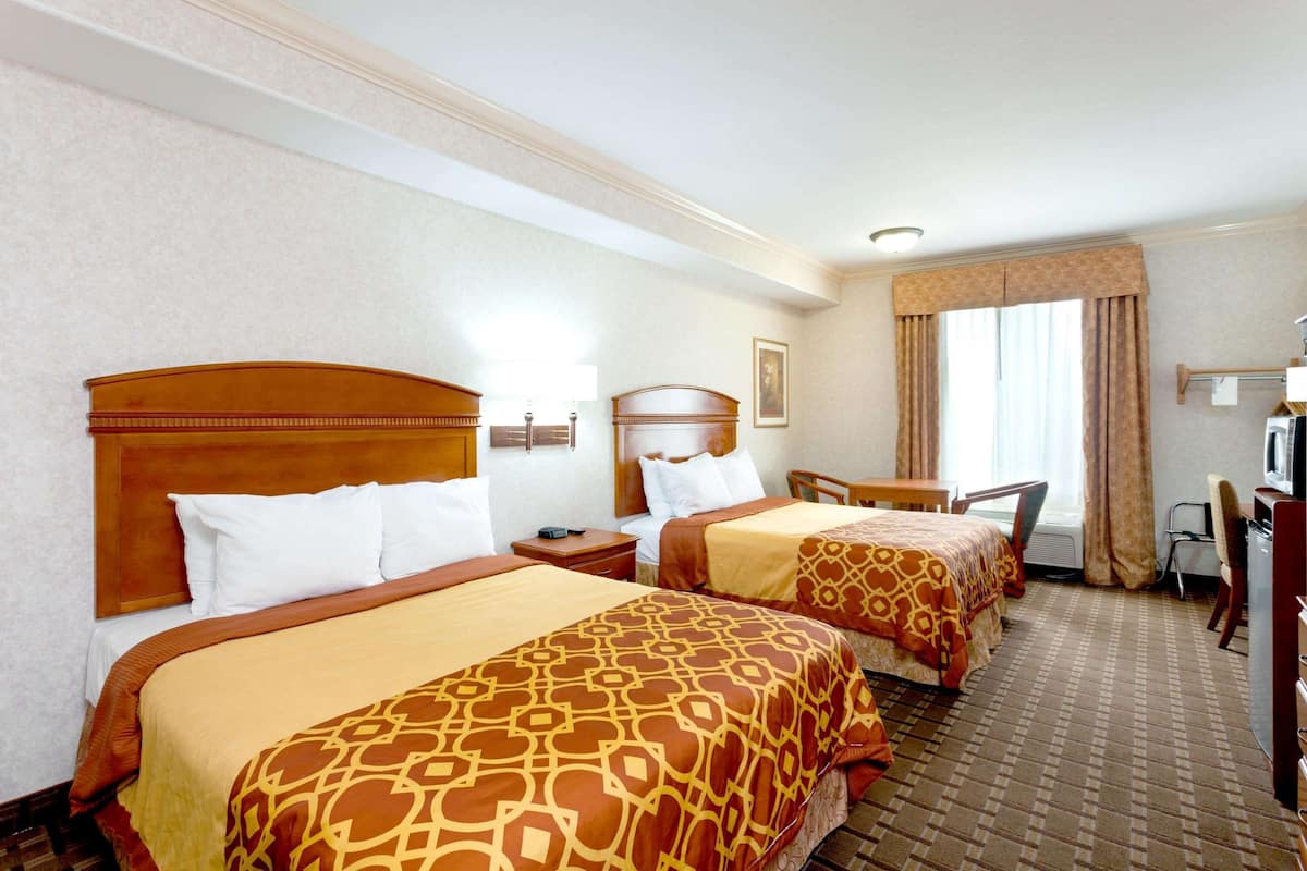A hotel room with two beds, a desk, a chair, and a television.