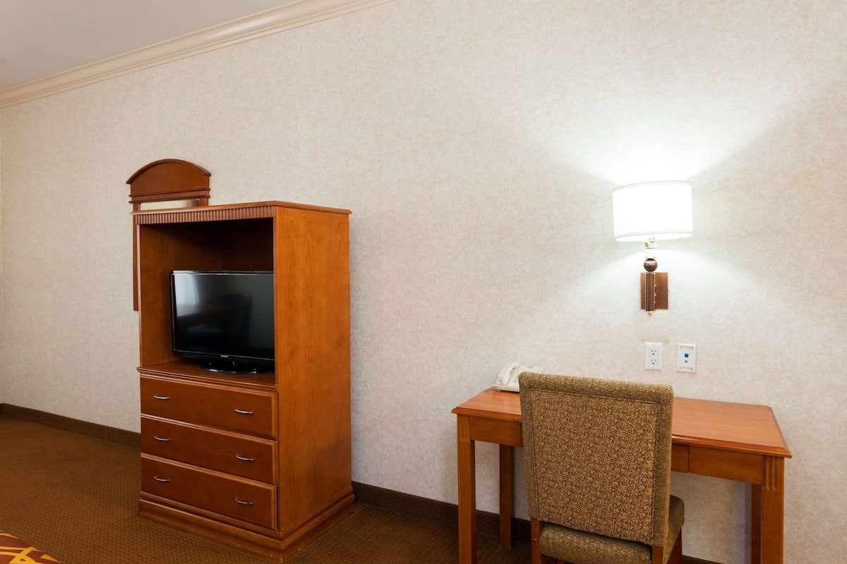 A hotel room with a wooden TV stand, a desk, and a patterned chair.