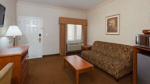 Hotelkamer met een gestreept sofa, een houten tafel, een televisie, een lamp, een deur en een airconditioner.