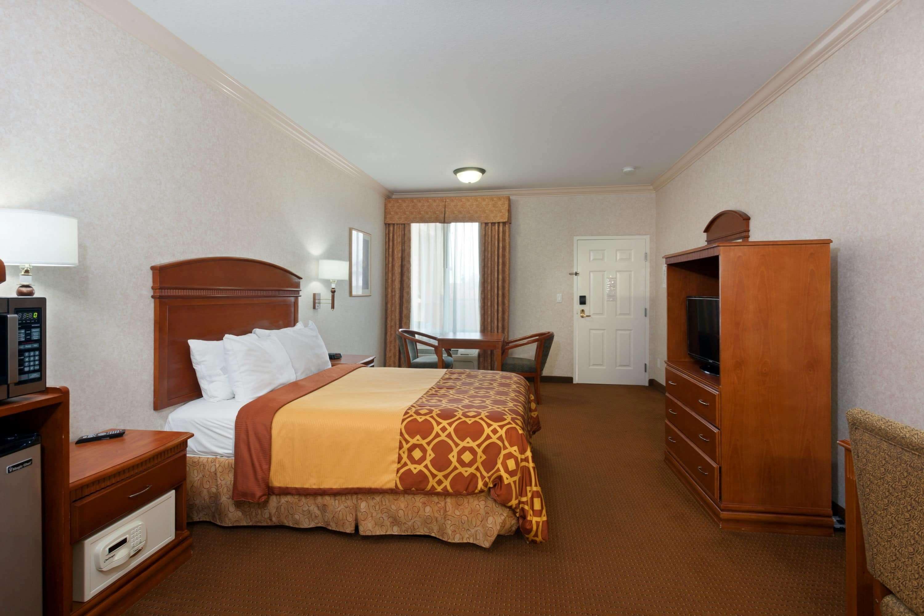 A hotel room with a bed, a desk, a television, a dresser, and a window with curtains.