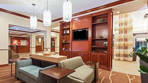 A hotel lobby with a reception desk, seating area, wooden paneling, a flat-screen TV, and a large potted plant. - Hilton Garden Inn Corpus Christi (Corpus Christi)