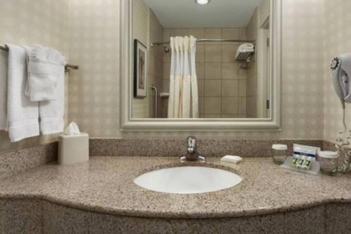 A bathroom with a sink, mirror, shower, and towel rack.