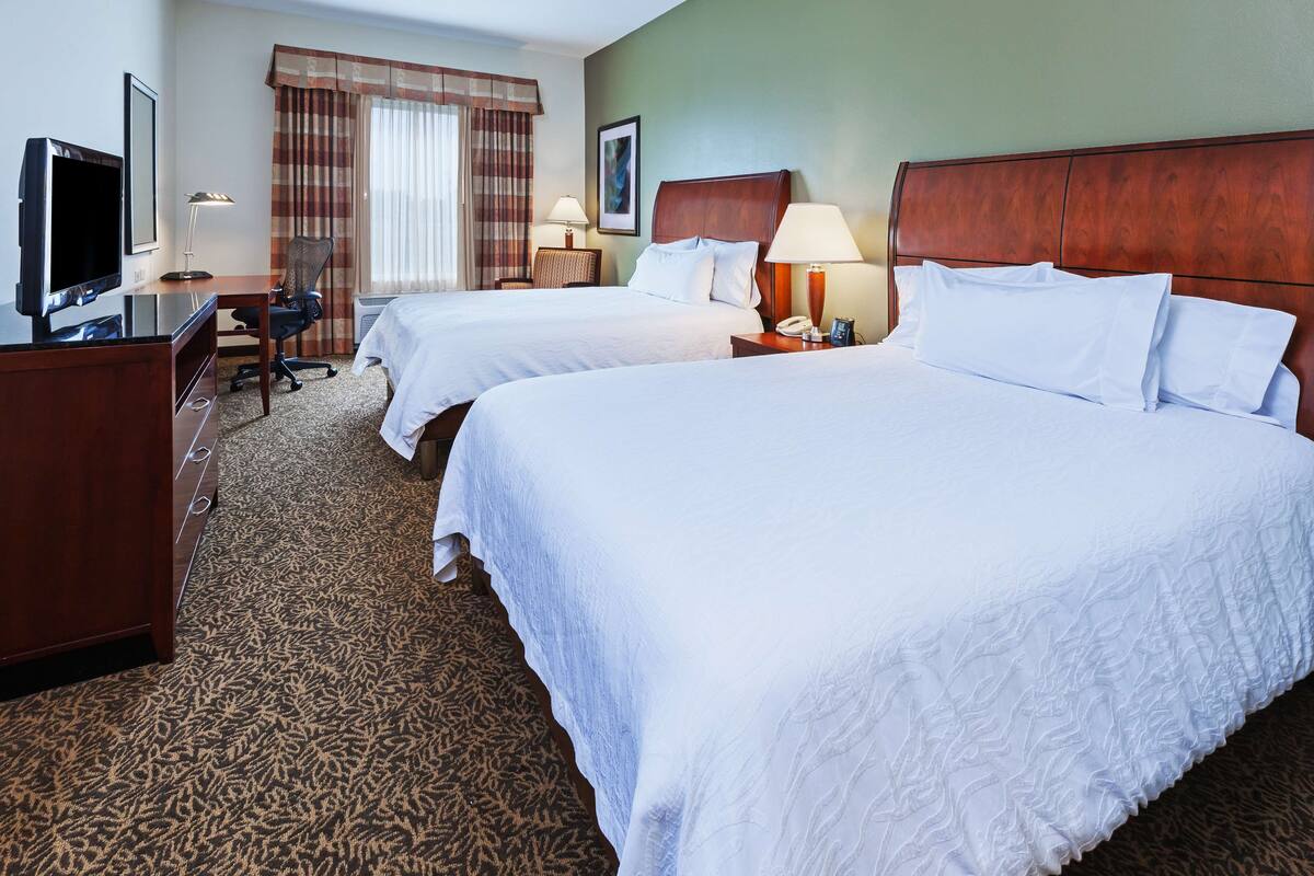 A hotel room with two beds, a desk with a computer, a chair, and a television.