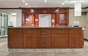A hotel reception area with a marble counter, wooden paneling, and a check-in/out sign. - Hilton Garden Inn Corpus Christi (Corpus Christi)