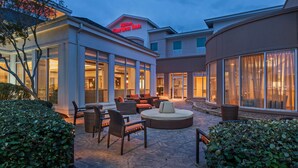 A well-lit outdoor patio area with seating and a large window overlooking the interior of the hotel. - Hilton Garden Inn Corpus Christi (Corpus Christi)