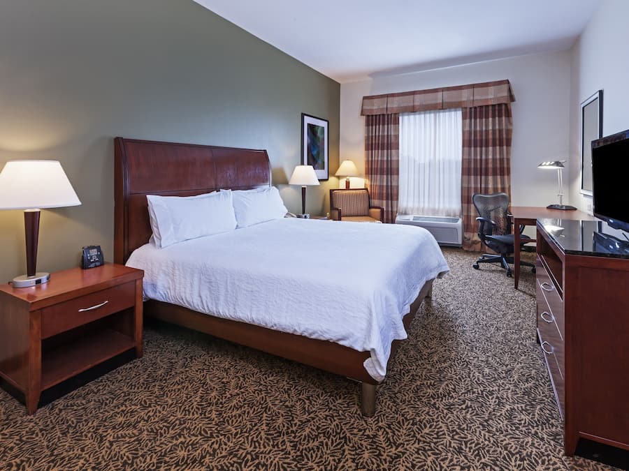 A hotel room with a large bed, two bedside tables with lamps, a desk with a chair, and a television.